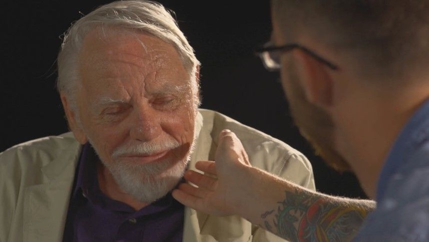 A young man is tracing his hand over an older man's face during a FaceAge encounter.