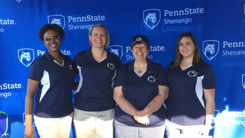 Four women pose for a picture in front of a Penn State Shenango drop cloth at last year's golf fundraiser.