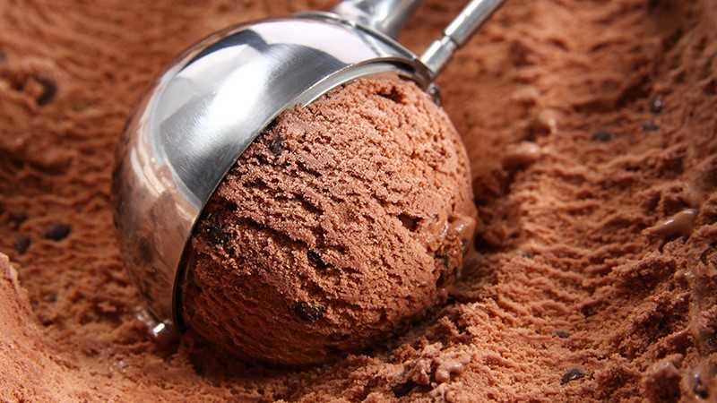 A tub of chocolate ice cream and a silver scooper.