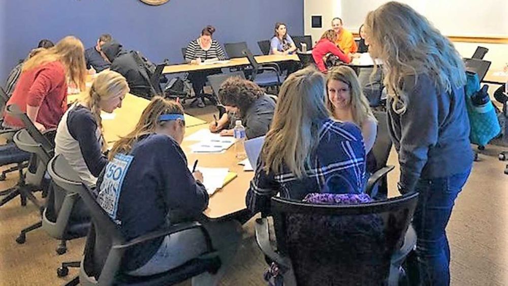 A group of students in a large classroom discussing their classroom project.