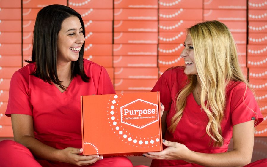 Two females holding one of their new boxes which contain items for the elderly