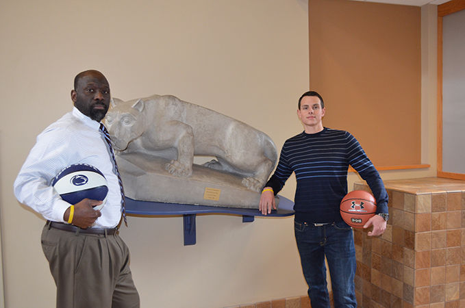 Two Penn State staff members standing with basketballs next to the Nittany Lion located in the campus' atrium area