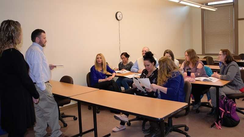 Two people stand in front of a classroom full of students and faculty members