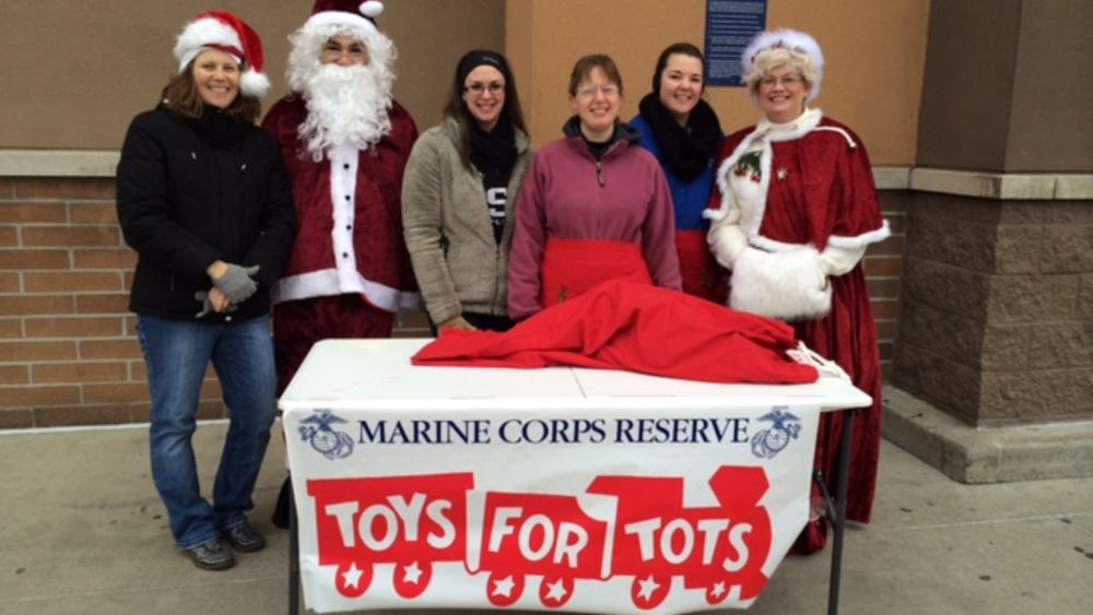 Penn State Shenango students and faculty standing in back of a table with a Toys for Tots sign. Two dressed up like Mr. and Mrs. Santa Claus.