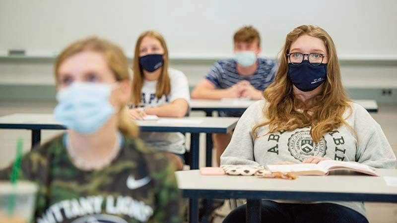 Three students wearing masks in socially distanced pattern in classroom