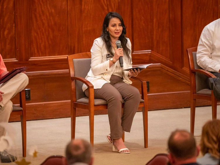 Assistant Professor of Cybersecurity Dima Rabadi seated onstage speaking into a microphone to a crowd of people