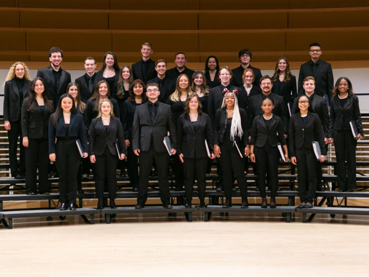 Choir ensemble Essence of Joy standing on a riser platform posing for a group photo.