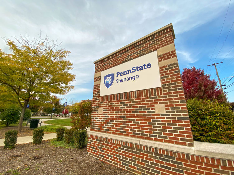 Penn State Shenango brick sign with yellow, green, and red trees in background