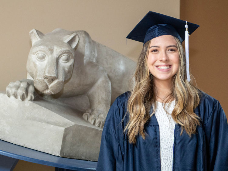 Rachel Maynard in cap and gown next to small Nittany Lion Shrine.