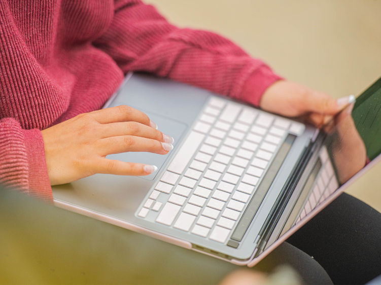 Close up of student sitting with laptop on their lap using the touch pad