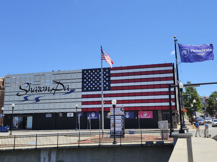 Exterior of a building with an American flag painted on the side and text saying Sharon, PA with sidewalks and flag poles in the foreground