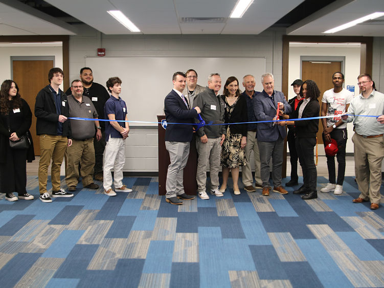 Students, faculty, staff and community members pose in front of a blue ribbon