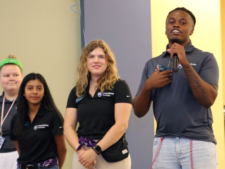 Four students standing on a stage, one is speaking into a microphone