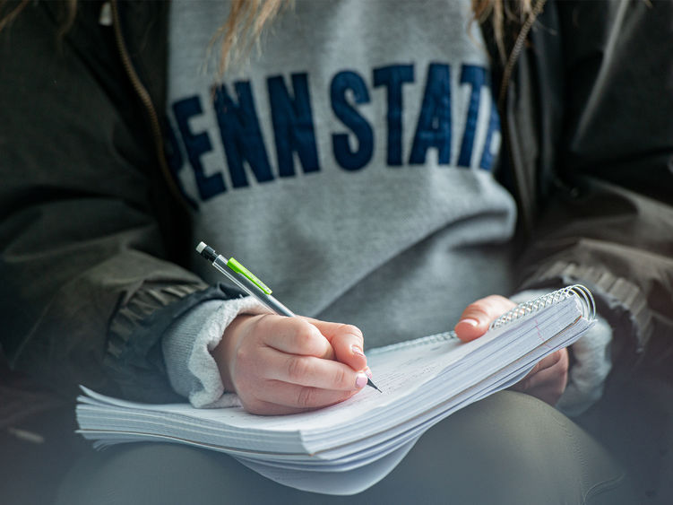 Student holding pencil writing in a notebook