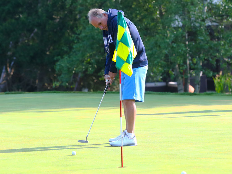 Golfer hits a golf ball towards a hole with a flag