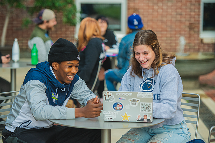 Two students working on laptop in a campus courtyard. 