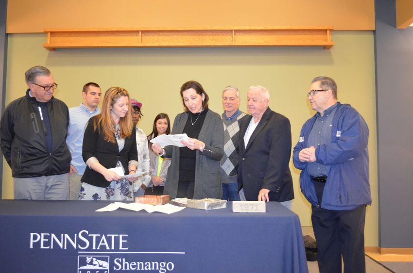 Dr. Jo Anne Carrick and Mandy Eagler, SGA president, open the campus' time capsule, while students and board members look on.